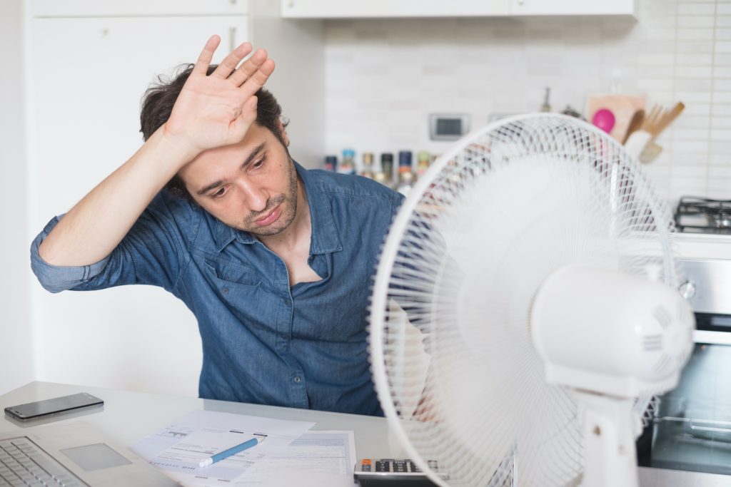 Mann der am Schreibtisch sitzt und dem heiß ist - eine Klimaanlage schafft Abhilfe für dieses Problem